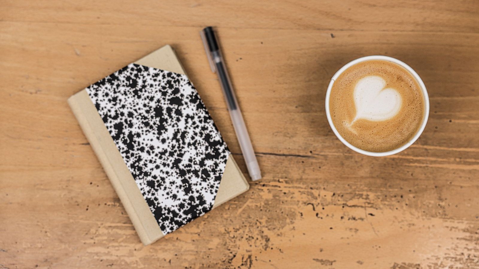 A pocket notebook open to a page of short dated lines, beside a coffee cup
