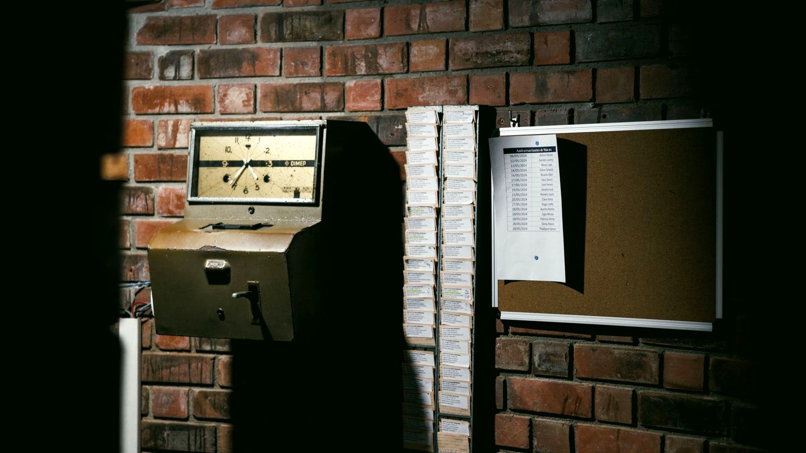 A time clock terminal on a warehouse wall with a printed schedule taped beside it