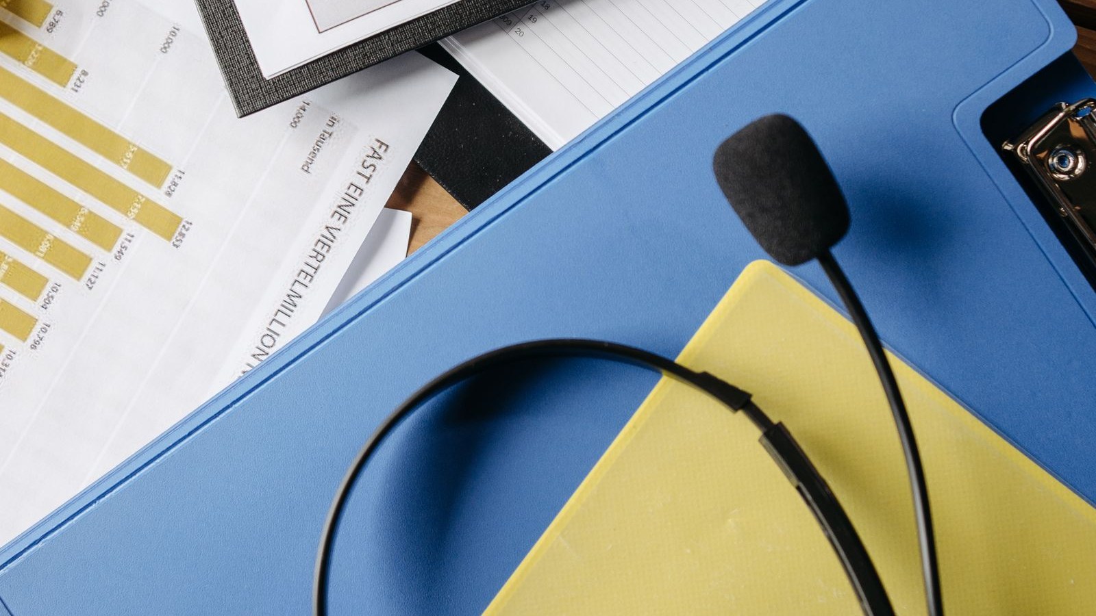 A headset resting on a desk beside a monitor showing a queue dashboard