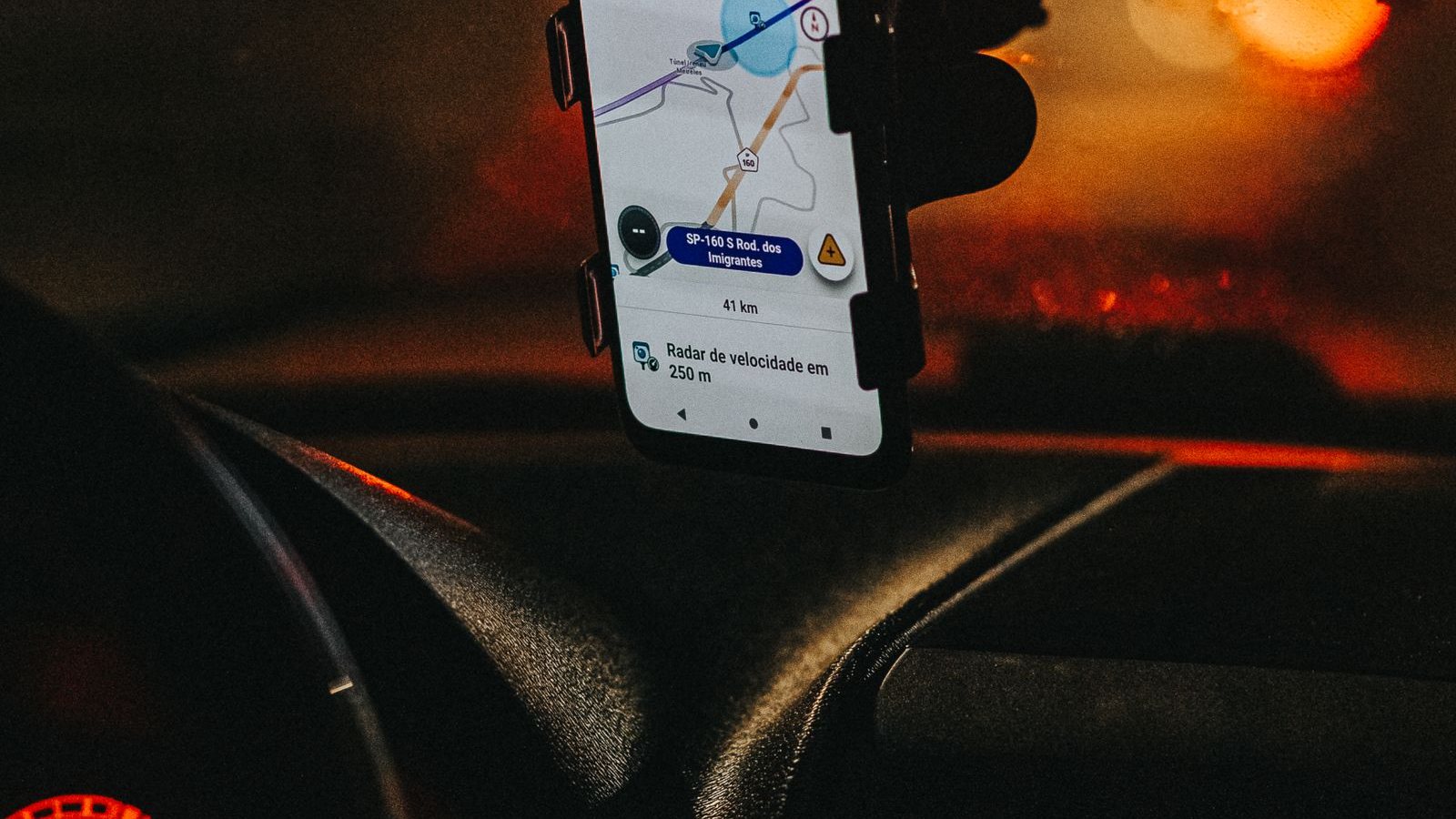 A phone mounted on a car vent showing a promotion banner, city street ahead