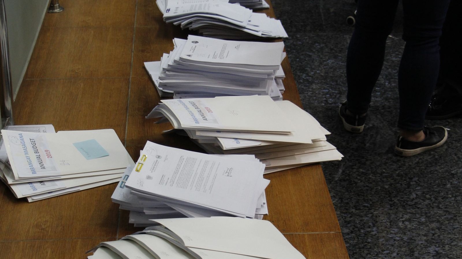 A stack of printed forms on a desk with a pen and an employee badge