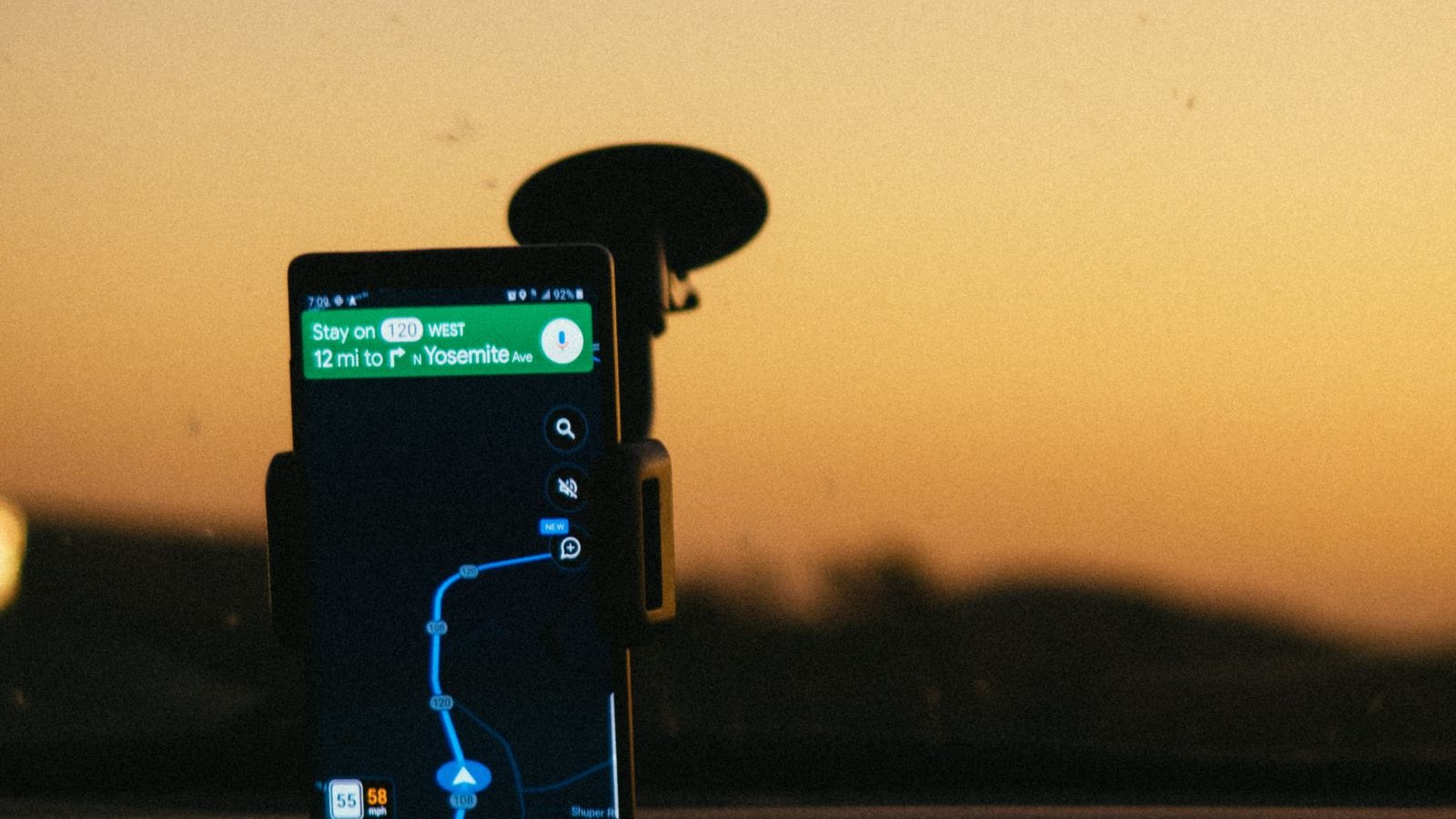 A parked car at dusk outside a lit storefront with a phone mounted on the dash
