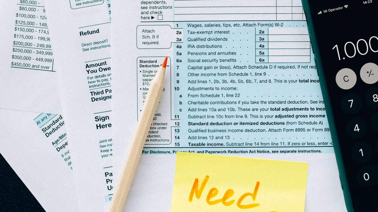 Open enrollment paperwork spread on a kitchen table beside a calculator and a phone